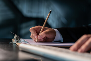 Closeup of office manager in suit holding a pencil with right hand, writing on a blank paper in the clipboard. Planning, office work, no face. Concept of contract