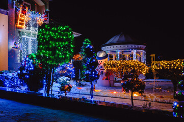 House Adorned with Christmas Holiday Lights and Decorations including Santa Snowman and Giant Trees Illuminated at Night. Christmas Lights outside on a House