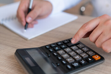 Top view of man office worker making a note in a notebook, pressing buttons on calculator on wooden office table desk. Closeup of male hands making a calculation, no face. Concept of calculation