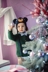 Little stylish boy decorates the Christmas tree. Cute baby indoors. The concept of Christmas, gifts, new year.