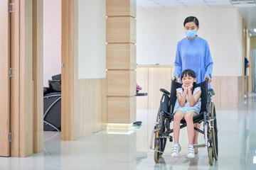 Smiling child patient girl sit on wheelchair with nurse in hospital