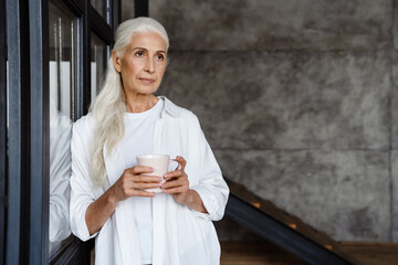 Senior woman drinking coffee near a window