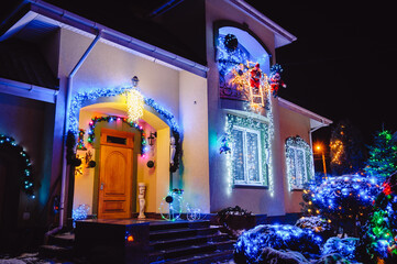 House Adorned with Christmas Holiday Lights and Decorations including Santa  and Giant Trees Illuminated at Night