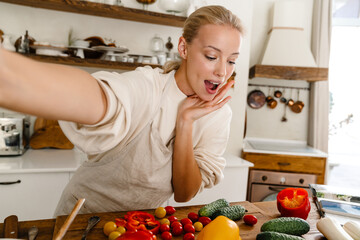 Astonished woman taking selfie and expressing surprise while making lunch