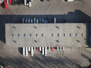 Aerial view of goods warehouse. Logistics center in industrial city zone from above. Aerial view of trucks loading at logistic center. View from drone.