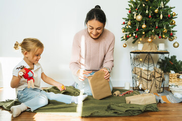 Fototapeta premium Mom and daughter packing Christmas gifts in room. Merry christmas and happy new year concept. Space for text. Family cozy moments.Morning before Xmas..