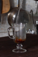 Pour boiling water into a glass of instant coffee in the kitchen. A man makes coffee at home.
