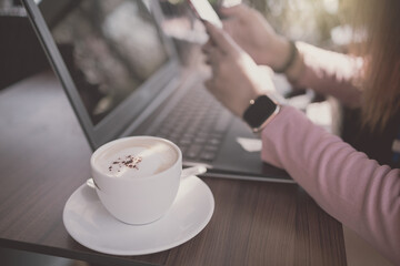 White coffee cup on wooden table with blurred computer notebook and women background. Drama tone.