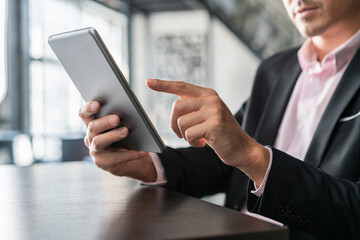 Businessman with grey digital tablet in hand, scrolling. Closeup of male hands with device in office room, businessman in black suit, usage of portable device indoors, concept of work