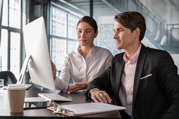 Male and female office managers discussing work, man in black suit and woman in white shirt. Business partners in office room looking at the computer screen, concept of teamwork