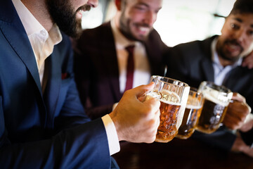 Happy young businessmen drinking beer and talking at pub after work