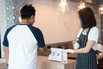 Fototapeta premium Asian waitress woman wearing face masks and holding an infrared thermometer and recommend customers to use hand alcohol sanitizer before entering the restaurant ( coffee shop ).