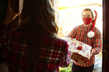 Delivery guy in Christmas outfit is giving parcel to a girl at the door while he is wearing face...