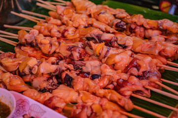 Close up raw squid meat skewer on banana leaf in the fresh market of thailand with spicy seafood sauce.Thailand street food