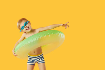 Portrait of smiling happy child boy in swimming goggles with neon inflatable rubber circle having fun isolated on yellow background. Summer vacation6 funny face