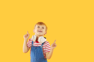 Smiling child boy enjoys listens to music in headphones over colorful yellow background. Vivid and fun emotions, happy child with pleasure listens to songs in wireless headphones..