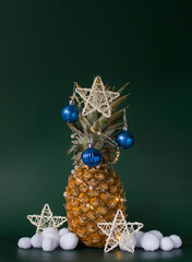 Christmas decor concept with pineapple, balls, stars and artificial snowballs on green background. Vertical. Copy space