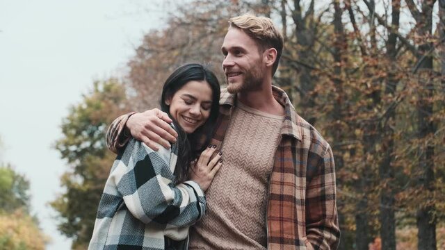 A smiling couple man and woman are hugging while walking in the autumn park