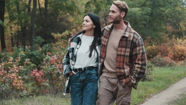 A pleased young couple man and woman are walking in the autumn park together