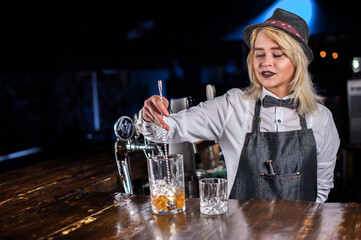Girl barman mixes a cocktail on the saloon
