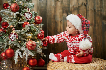 Little girl 1 year old in red costume touching christmas tree with red decorations