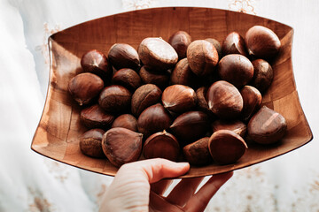 Close up of female hand holding raw chestnuts in wooden dish