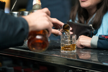 Barman hand pouring strong alcohol into a cocktail glass using a professional bartender tool on
