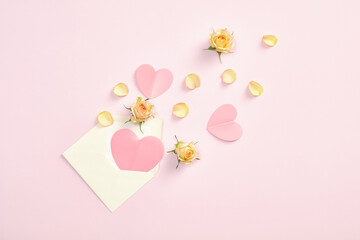 Envelope with pink paper hearts and roses flowers petals and buds on pastel pink background. Valentines day, love, romantic letter concept.