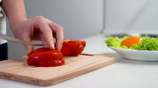 Cut vegetables on a wooden chopping Board close-up. Preparation of salad. Women's hands cut red pepper close-up, 4K video. Vegetarian salad.