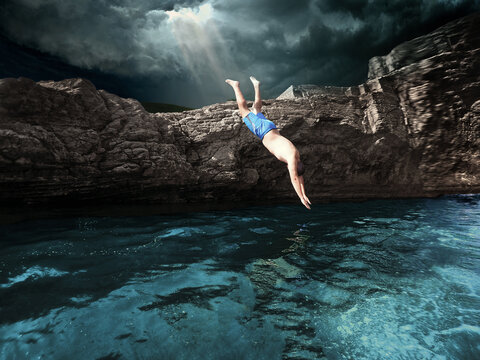 Man Diving In Sea By Rock Formation Against Sky