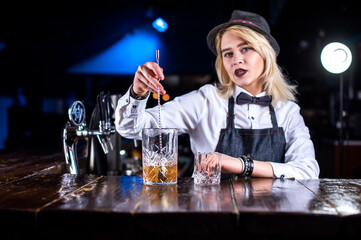 Focused girl bartending pouring fresh alcoholic drink into the glasses behind the bar