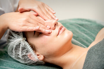 Young woman getting facial massage with closed eyes by beautician in beauty salon