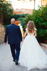 The newlyweds walk and smile, at the entrance to the castle against the background of a stone wall and palm trees.