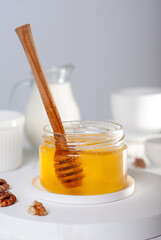 Flower honey in glass bowl with wooden dipper, milk and dishes on a white table