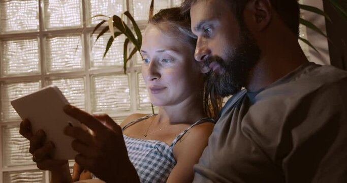 Caucasian young pregnant woman and her breaded husband looking ultrasound baby picture together on tablet at home.