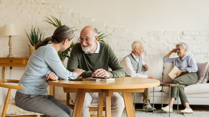 Elderly man and woman sitting at table and enjoying joyful talk, another senior couple...