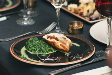 Baked chicken breast with creamy spinach on a dark ceramic plate. Comfort food in a restaurant