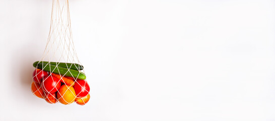 String bag with vegetables and fruits hanging on a white background.