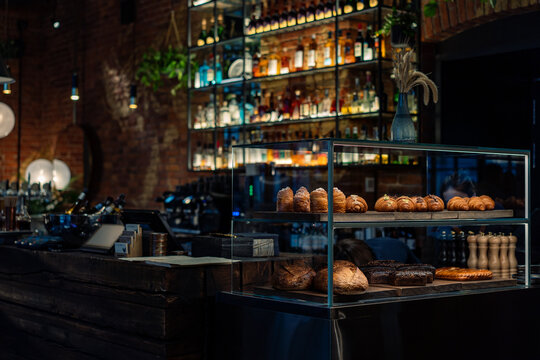 Bar counter with a pastry showcase in small restaurant. Bottles Of Alcohol And Spirits On Backlight Shelves on background. Image with selective focus