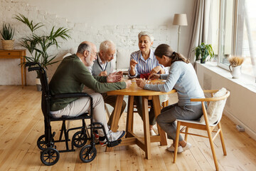 Group of four senior people, two men including disabled one and two women, sitting at table...