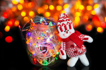 Colorful Christmas bokeh background with a toy snowman and a garland in a jar. Selective focus