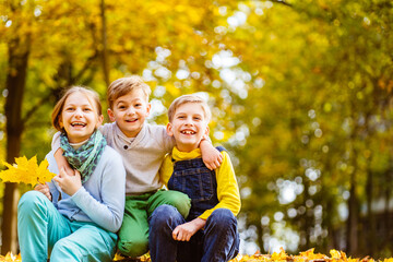 Fototapeta premium Portrait of three children of different age spending time together at autumn time by a forest or park looking at camera laughing. Positive emotions, enjoy childhood concept.