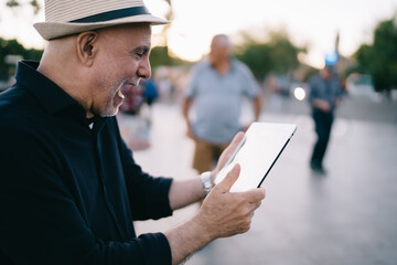 Surprised adult man in straw hat checking mail messages on touch pad and feeling excited, happy...