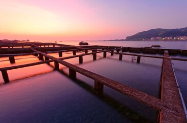 Obraz premium Beautiful sunrise scenery of a marine ranch (fish farming) in northern Taiwan, with peculiar artificial structures of aquaculture, fishing boats & islands on distant horizon under dramatic dawning sky