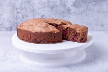 Chocolate pie with cherries on a white cake stand, one piece cut off. Homemade baking. Close-up.