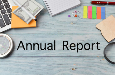 Top view of compass, laptop, memo note, banknote, notebook, alphabet beads, sticky notes, pen, board and magnifying glass on white background written with Annual Report. Business and financial concept