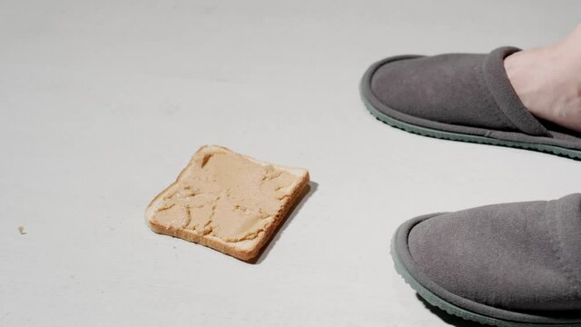 Peanut butter toast falls down on a floor near a slippers. Slow motion.