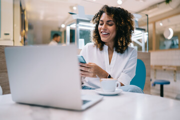 Joyful woman with candid smile on face using smartphone application for online messaging in social networks, happy freelancer checking mobile notification for installing to digital cellular technology