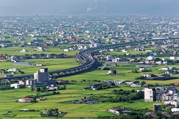 A curved highway through the green rice fields with houses scattered throughout the plain in Yilan, Taiwan ~ Aerial view of National Freeway No.5, Taipei-Ilan Section in Ilan, Taiwan, Asia