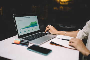 Unrecognizable female It professional working with displayed graph charts editing web information during freelance distance job, cropped woman checking data infographics on modern laptop computer